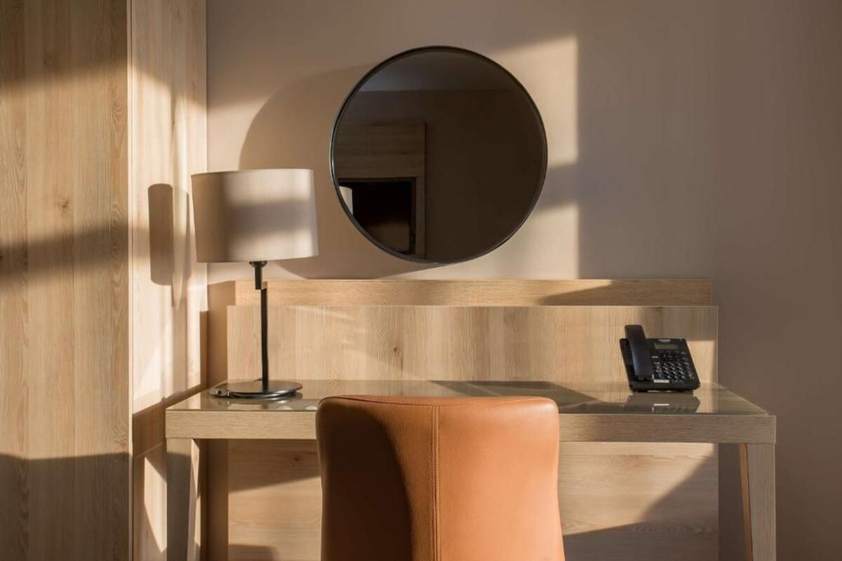 Een hotelkamer met een houten bureau, een ronde spiegel, een lamp en een telefoon.