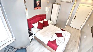 A bedroom with a red headboard, a bed with white and red bedding, a small bedside table, a wall-mounted air conditioner, and a door. - Taksim Capital Hotel (Istanbul)