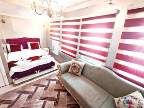 Ein Hotelzimmer mit Bett, einer Couch, einem Chandelier und gestreiften Jalousien.