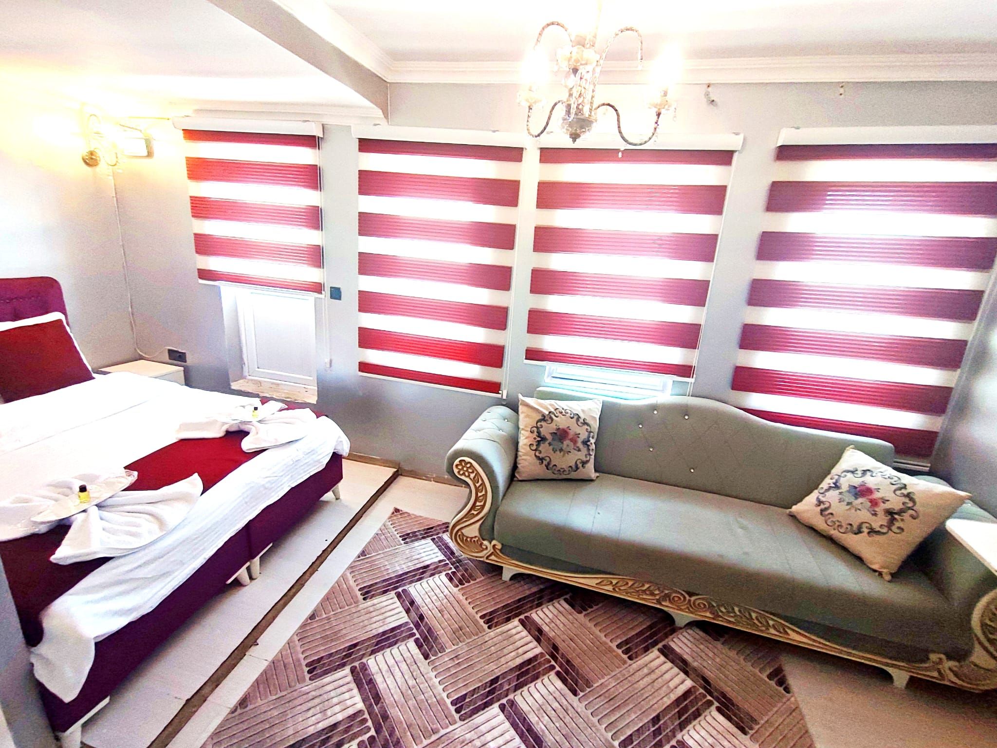 A hotel room with a bed, a sofa, a chandelier, and striped curtains.