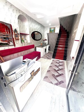A compact living space with a red sofa, a white cabinet, a washing machine, and a staircase with a red carpet. - Taksim Capital Hotel (Istanbul)