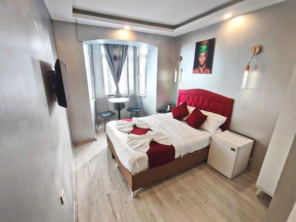A modern hotel room with a large bed, a small bedside table, a chair, a table, and a window with curtains. - Taksim Capital Hotel (Istanbul)
