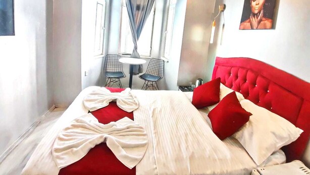 A hotel room with a red upholstered bed, a white blanket, and a red pillow. There is a small round table with two chairs in the corner. - Taksim Capital Hotel (Istanbul)