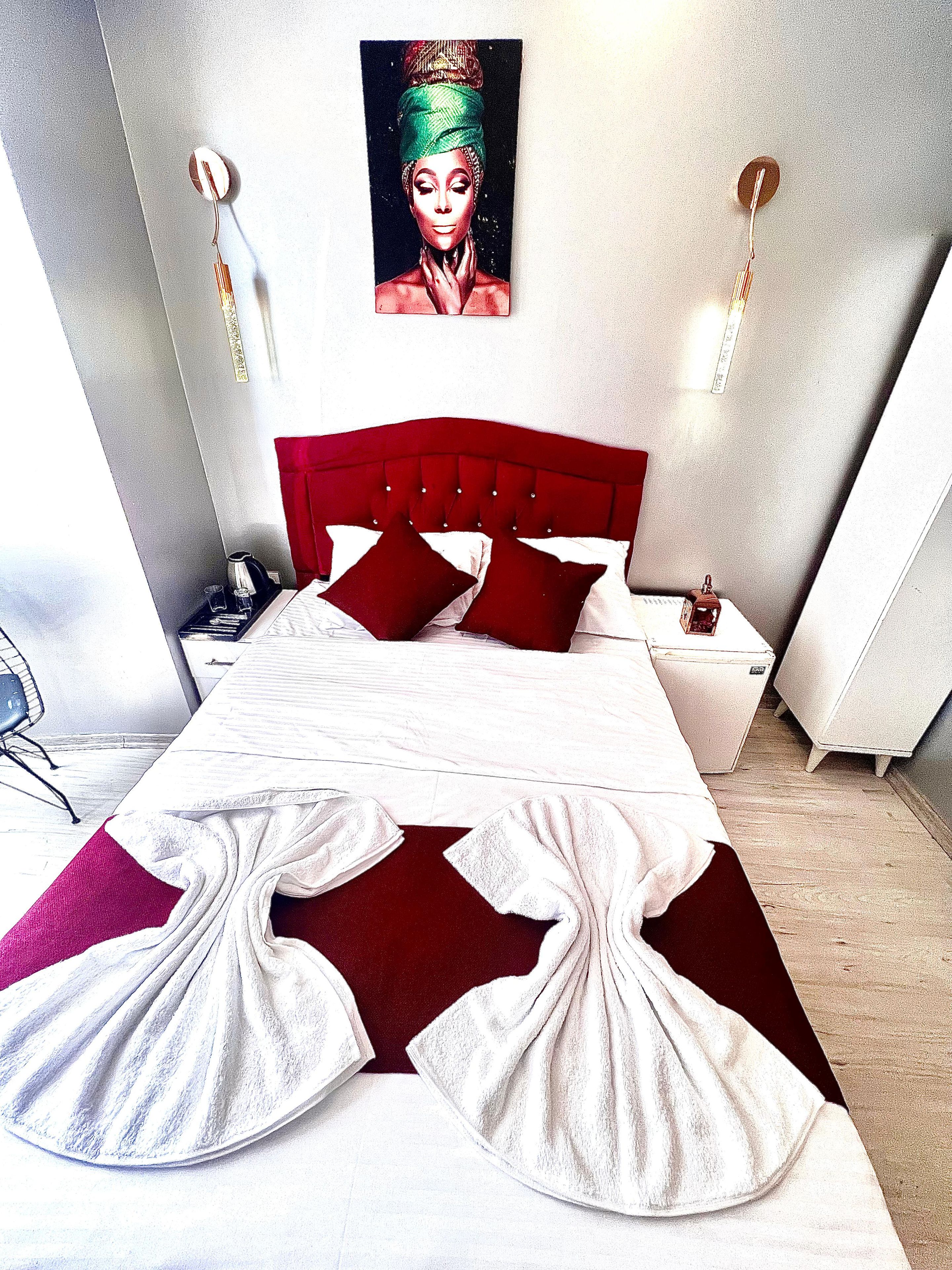 A modern hotel room with a large bed, red and white bedding, a painting on the wall, and a red and white rug.