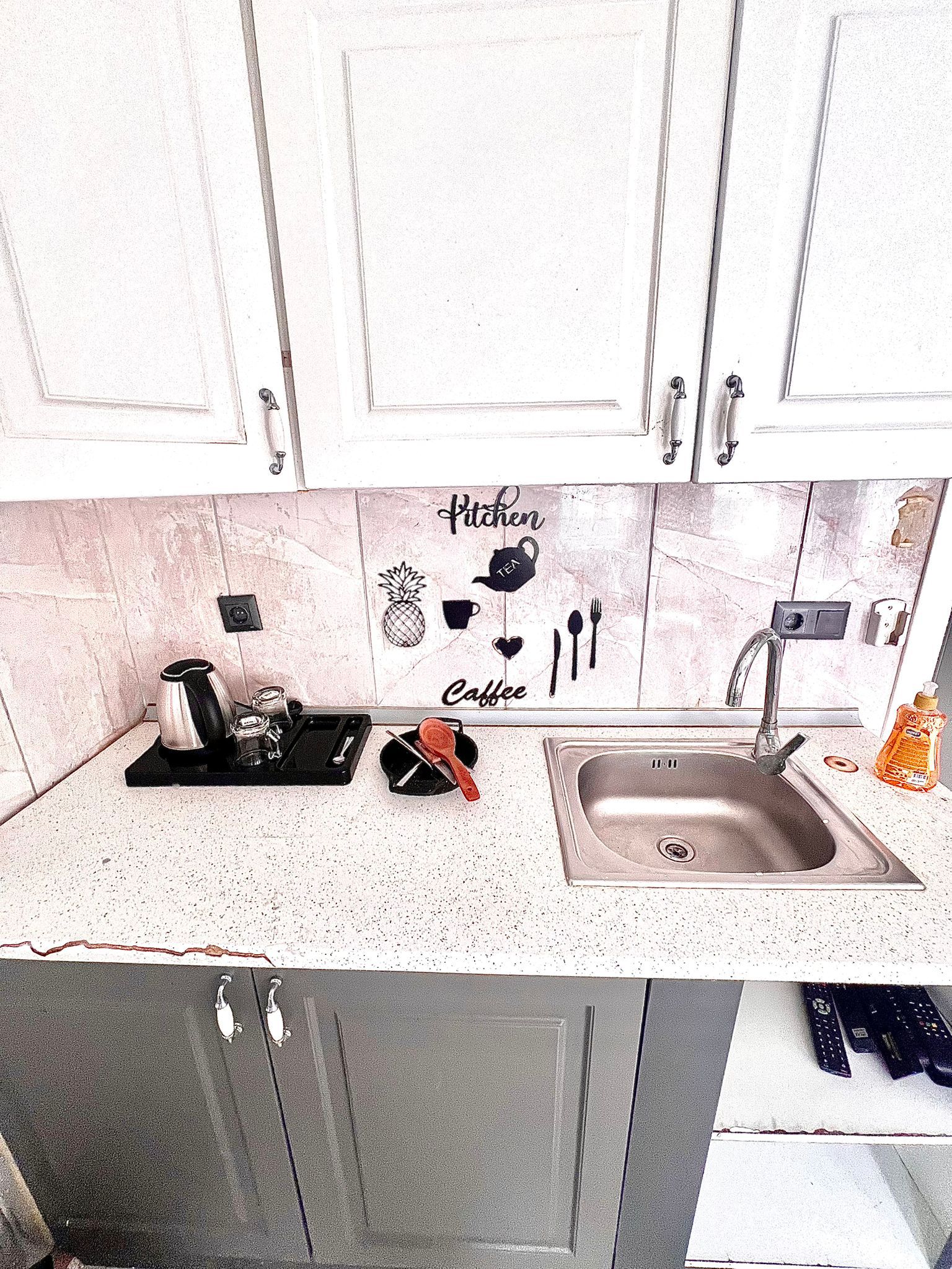 A kitchen with white cabinets, a granite countertop, and a sink. There are kitchen utensils and a coffee maker on the counter.