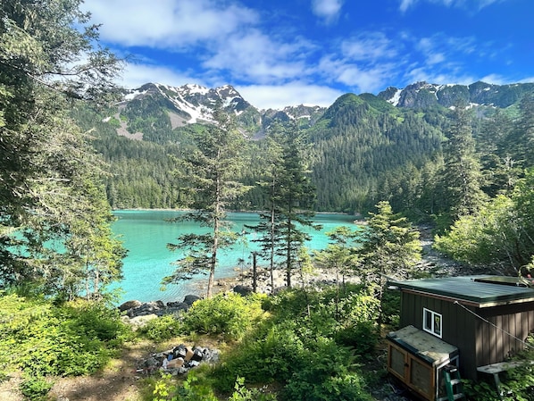 A cabin with a view of a turquoise lake surrounded by dense forest and mountains.