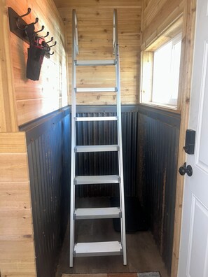 A metal ladder in a corner of a room with wooden walls and a window.