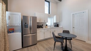 A modern kitchen with stainless steel appliances, white cabinets, a dining table with chairs, and a window above the sink. - Cozy Den - Minutes to Downtown Denver and near Red Rocks (Denver)