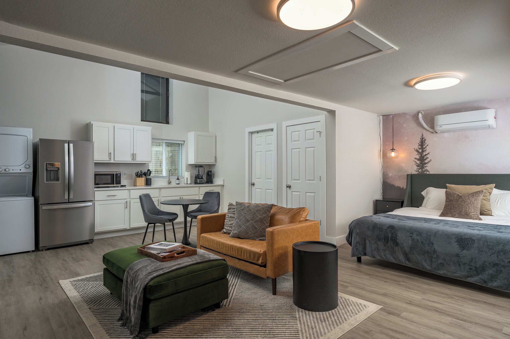 A modern, compact living space with a kitchenette, a sofa, a bed, and a trash can.