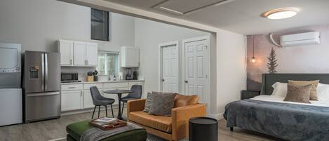 A modern, compact living space with a kitchenette, a sofa, a bed, and a trash can.