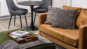 A cozy living room with a brown leather sofa, a wooden side table with a tray of books, and two black chairs around a small round table. - Cozy Den - Minutes to Downtown Denver and near Red Rocks (Denver)