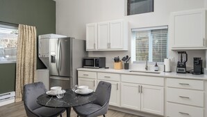 A compact kitchen with white cabinets, a refrigerator, a microwave, and a coffee maker. There is a dining table with two chairs and a window with blinds. - Cozy Den - Minutes to Downtown Denver and near Red Rocks (Denver)
