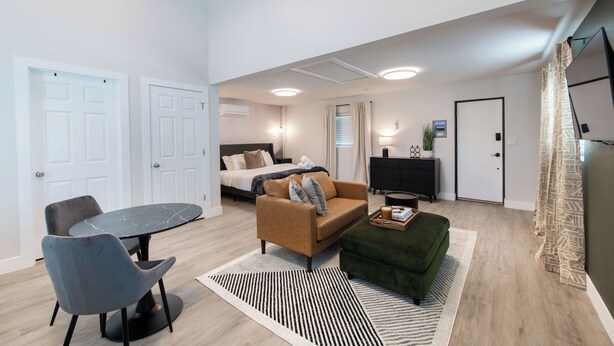 A modern hotel room with a bed, a sofa, a dining table with chairs, a TV, and a small desk. - Cozy Den - Minutes to Downtown Denver and near Red Rocks (Denver)