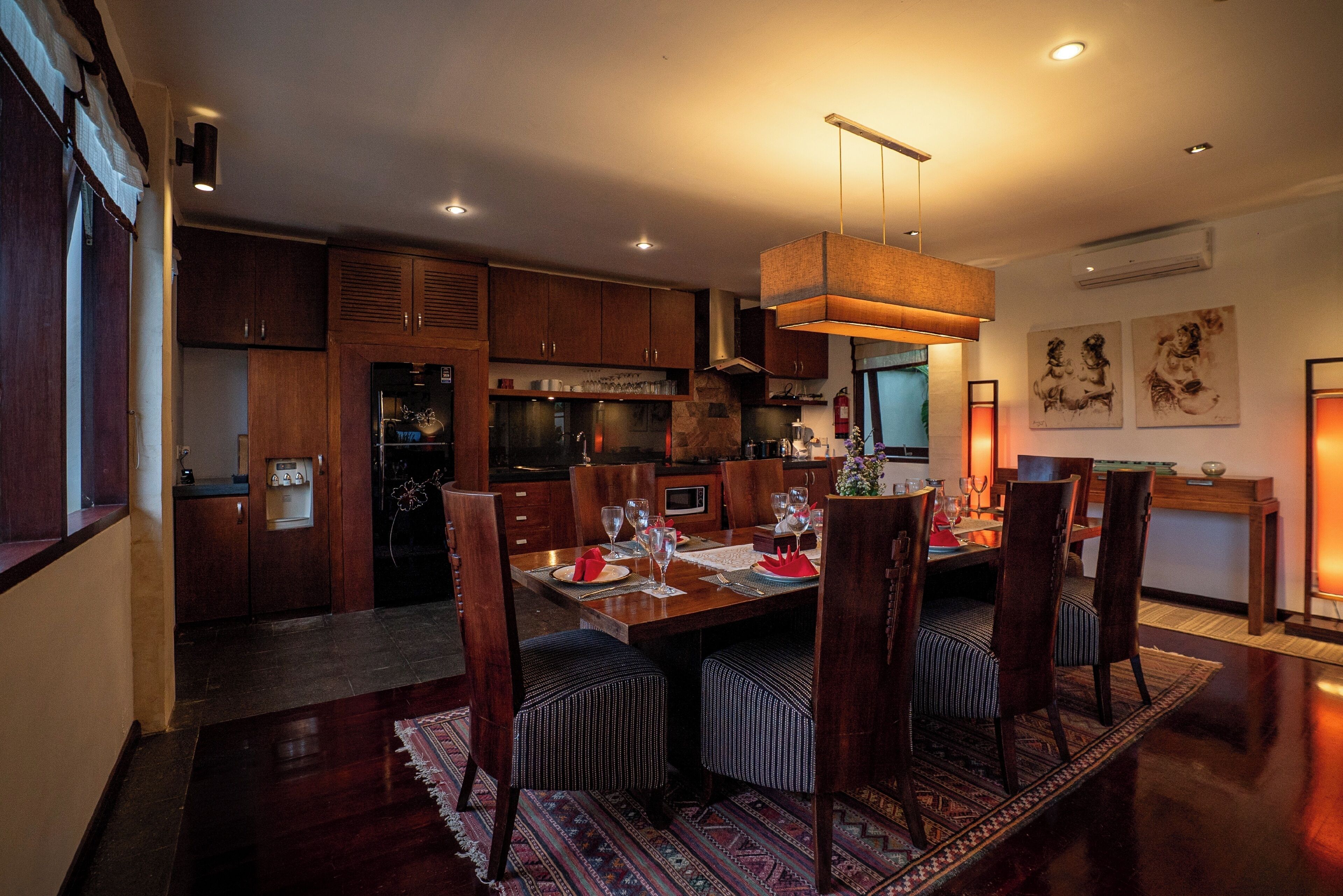 A modern kitchen with wooden cabinets, a dining area with a table set for four, and a patterned rug on the floor.