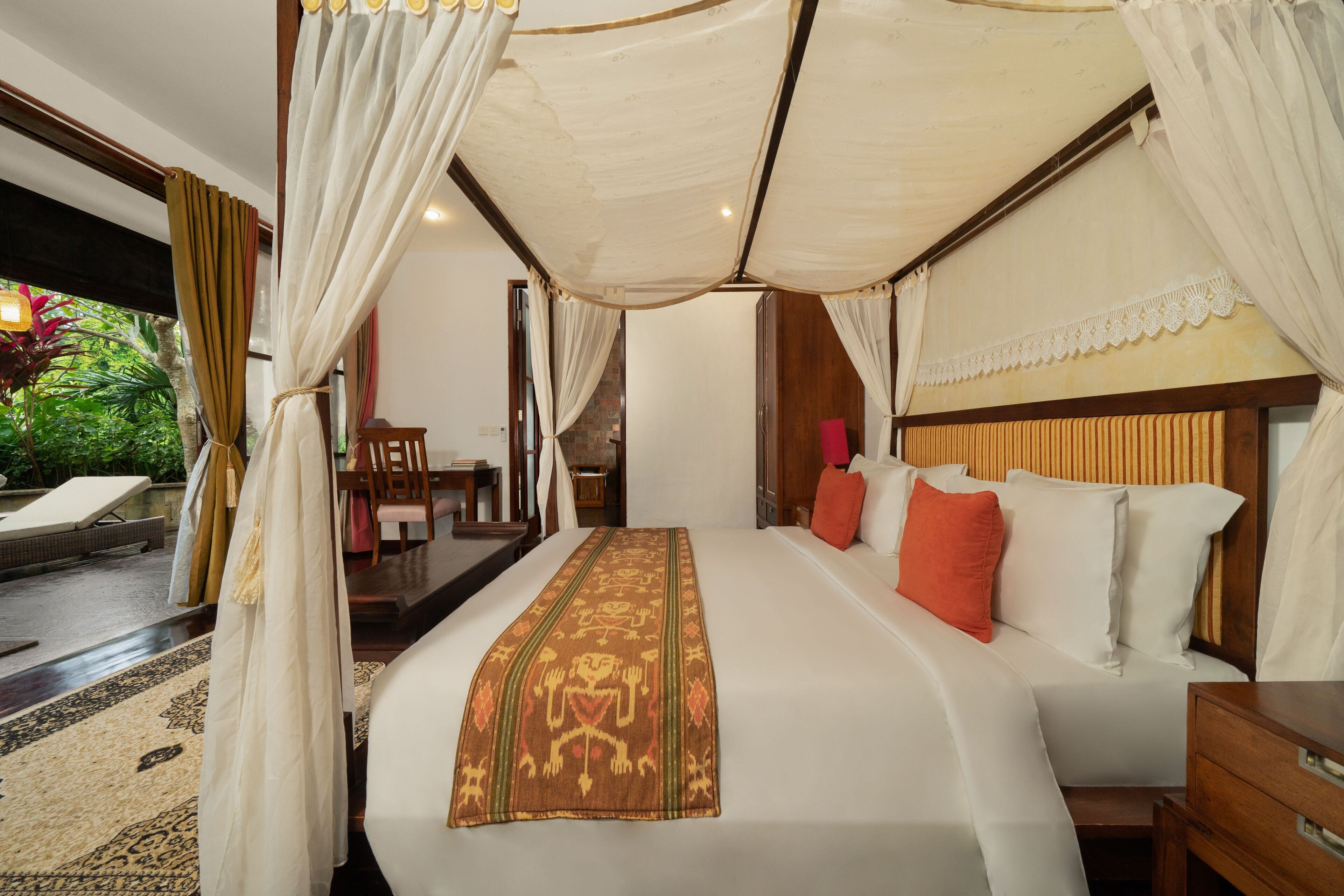 A spacious bedroom with a large bed, a canopy, and a view of a lush garden.