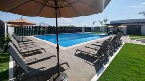 A swimming pool with lounge chairs and umbrellas, surrounded by a fence and greenery. - Casa Primavera (Puerto Vallarta)