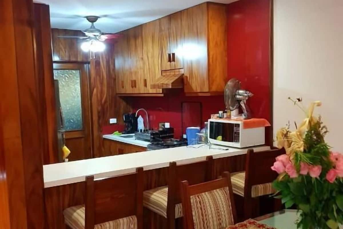 Una cocina con armarios de madera, un microondas y una zona de comedor con sillas y una mesa.