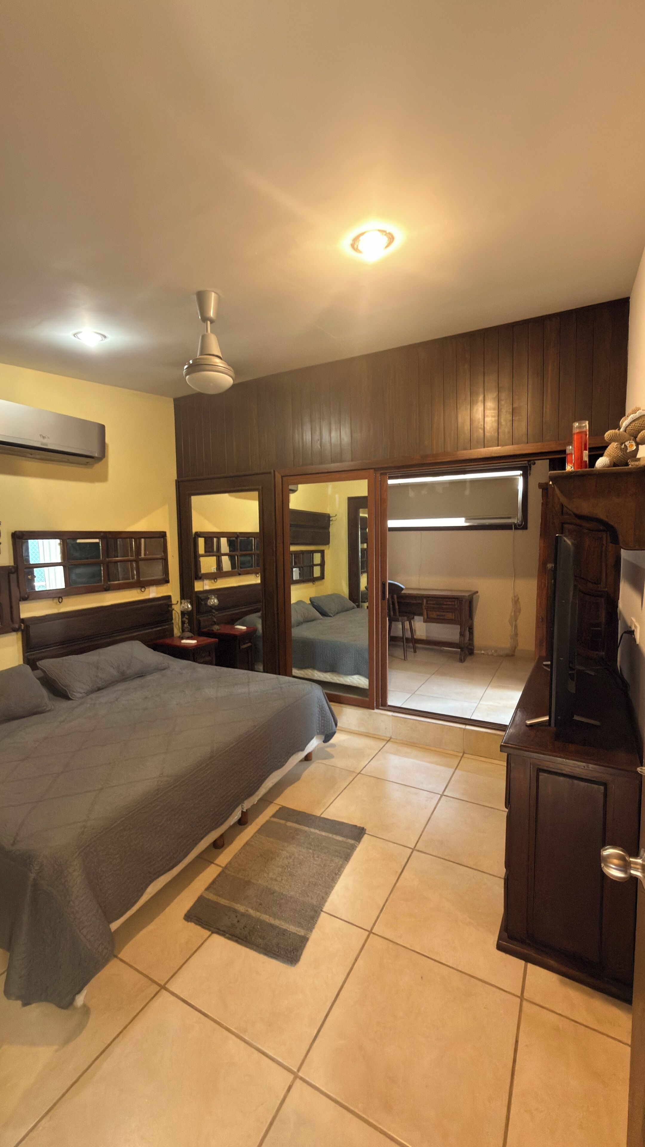 A bedroom with a bed, a desk, a chair, a TV, and a ceiling fan.
