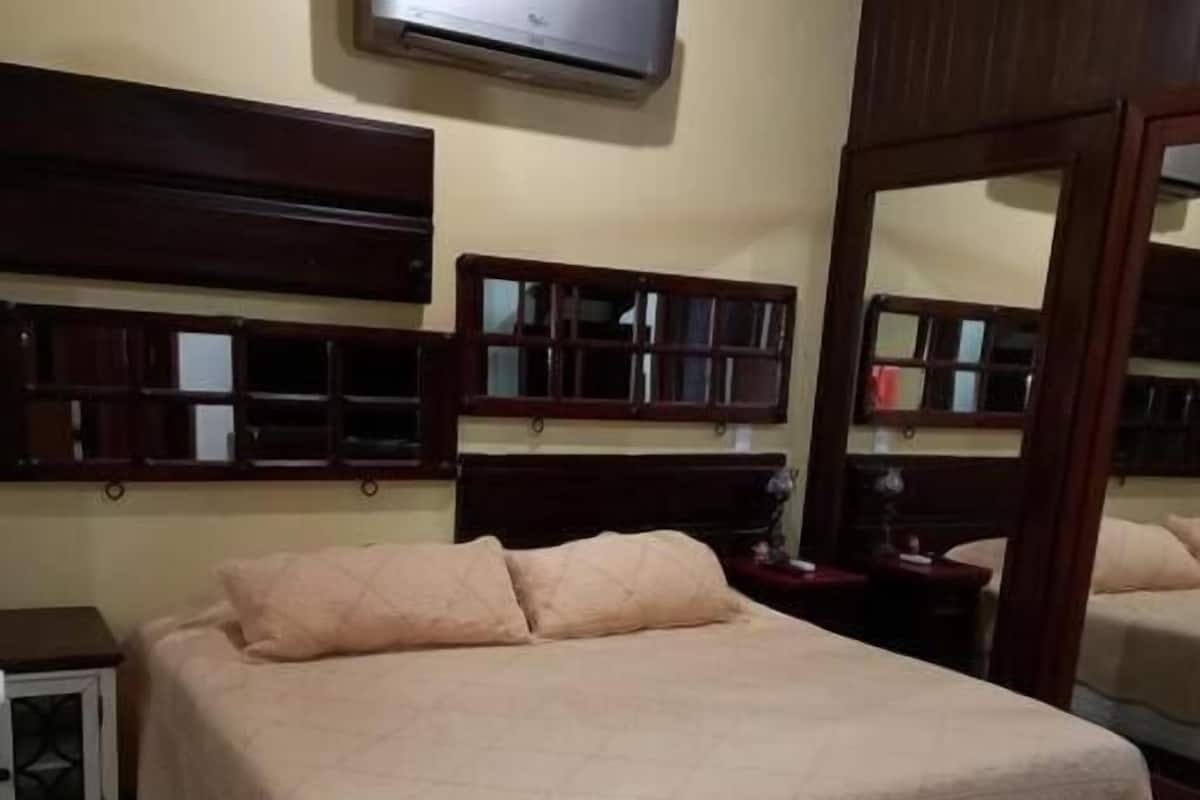Un dormitorio con una cama grande, una mesita de noche, un aire acondicionado de pared y un espejo.