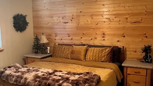 Ein Schlafzimmer mit Holzwand, Deckenventilator, Bett mit Felldecke, Nachttisch und einem kleinen Weihnachtsbaum.