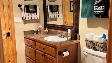 A bathroom with wooden cabinetry, a white sink, a large mirror, and a toilet.