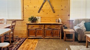 Ein gemütliches Blockhaus-Interieur mit Holzwänden, einem Essbereich, einer Küche mit Holzausstattung und einem Deckenventilator.