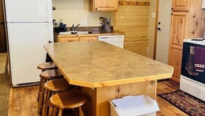 Eine Küche mit Holzausstattung, einem weißen Kühlschrank, einer großen Kochinsel mit Hockern und einem Mülleimer.