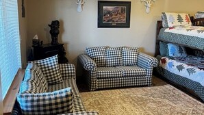 Ein Wohnzimmer mit einem gestreiften Sofagarnitur, einem gemusterten Teppich und einem Bett mit Bettwäsche im Waldmotiv.