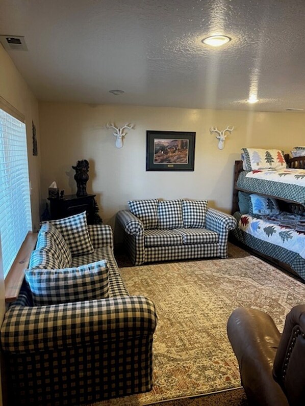 A living room with a checkered sofa set, a patterned rug, and a bed with a forest-themed bedspread. - Scofield Shores • Sunset Lake Views • Walk to Water • Sleeps 10 (Scofield)