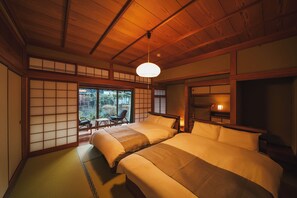 Quarto japonês tradicional com chão de tatame, duas camas, uma porta deslizante e vista para um jardim.