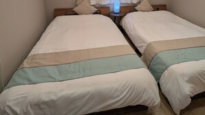 Ein Schlafzimmer mit zwei Betten, einem Nachttisch, einer Lampe und einem Fenster mit Vorhängen.