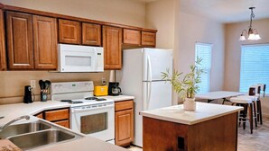 A kitchen with wooden cabinets, a white stove, a refrigerator, and a dining area with a table and chairs. - 3-bedroom townhome in pleasant Mesquite with AC for relaxing stays (Mesquite)