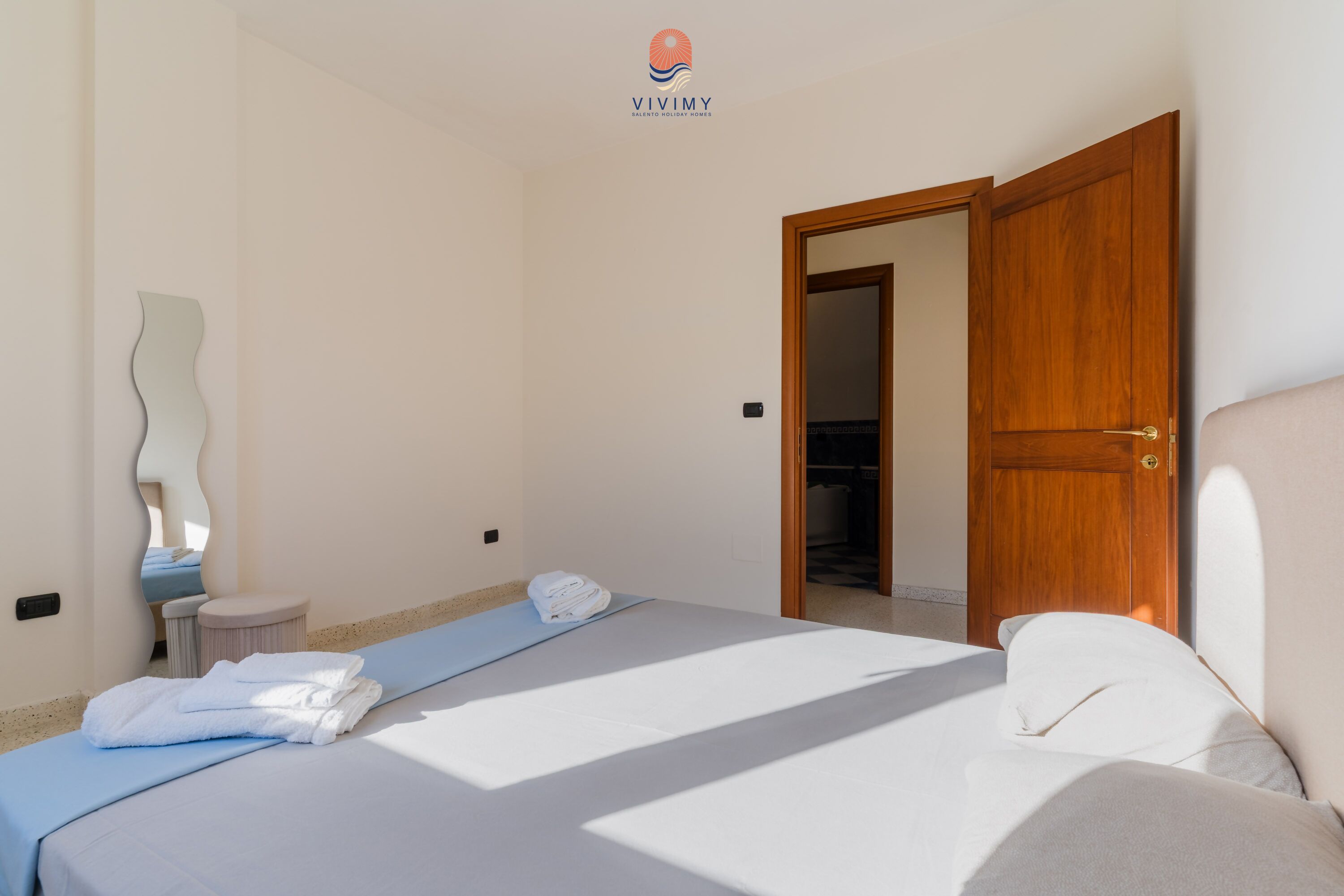 A hotel room with a bed, a wooden door, a mirror, and a towel rack.