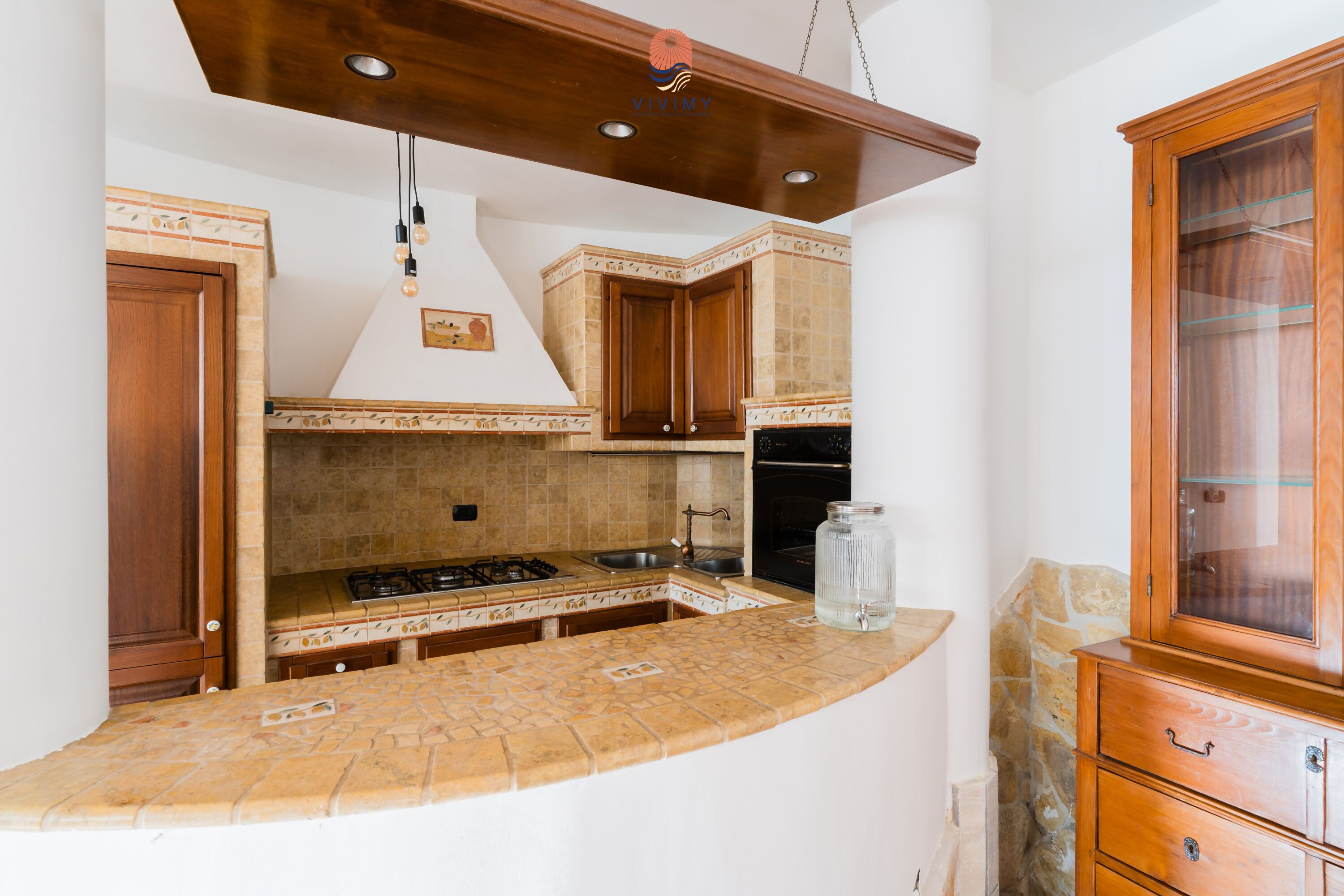Eine Küche mit gewölbter Arbeitsplatte, Holzschränken, einem Gasherd und einem eingebauten Backofen.