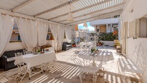 An outdoor patio with a table set for dining, surrounded by white furniture and decorative elements. - White Queen by Vivimy (Gallipoli)