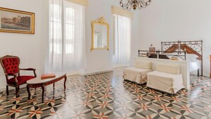 A room with a patterned floor, a red upholstered chair, a white sofa, a bed with a metal frame, and a large mirror on the wall. - White Queen by Vivimy (Gallipoli)