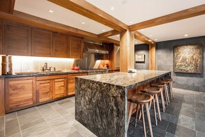 A modern kitchen with wooden cabinets, a granite island, bar stools, and a stone backsplash. - Vail Village Walk to Ski, 12ppl, Sebastian Access (Vail)