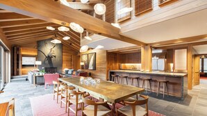 Un grand espace à manger avec une longue table et des chaises en bois, une cuisine avec un bar et une cheminée.