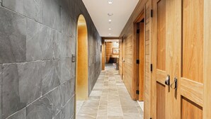 Un couloir aux murs de pierre sombre, aux portes en bois et au sol carrelé.