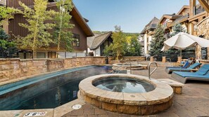 A pool area with a hot tub, lounge chairs, and a stone wall. - Vail Village Walk to Ski, 12ppl, Sebastian Access (Vail)