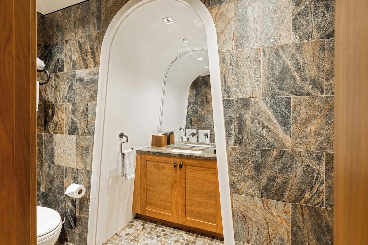 A bathroom with a marble wall, wooden cabinets, and a white sink.