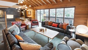 Un vaste espace de vie doté d’un plafond en bois, de grandes fenêtres et d’un agencement varié comprenant des canapés et des fauteuils.