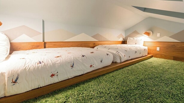 Une chambre avec un lit superposé, une moquette verte et un motif géométrique sur le mur.
