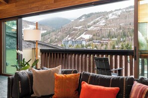 Ein Balkon mit Blick auf eine Berglandschaft, eine Couch mit Kissen und ein Tisch mit Stühlen.