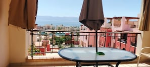 Un balcon avec une table et des chaises, donnant sur un paysage urbain le long de la côte.