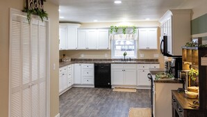 A spacious kitchen with white cabinets, a black dishwasher, and wooden flooring. - Mimosa Bungalow - Mimosa Bungalow (Crane)