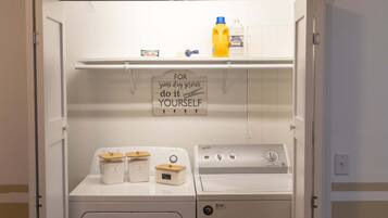 A laundry room with a washing machine, dryer, and detergent bottles on the shelves.