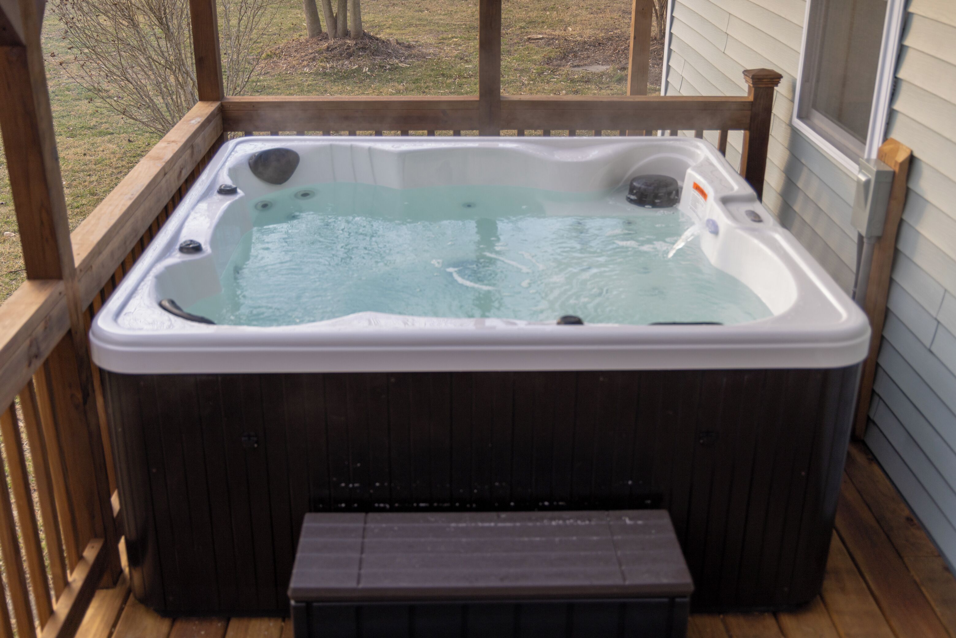 A hot tub on a wooden deck with a view of a grassy yard.