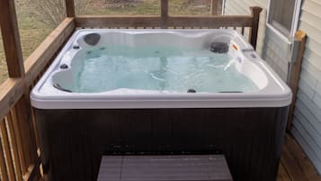 A hot tub on a wooden deck with a view of a grassy yard.