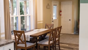 A dining area with a wooden table, four chairs, and a window with curtains. - Mimosa Bungalow - Mimosa Bungalow (Crane)